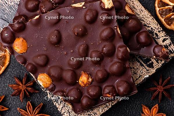 Food, Black bitter chocolate with whole hazelnuts, candied fruits and mint, broken into pieces on a dark concrete background [IBR124773741]