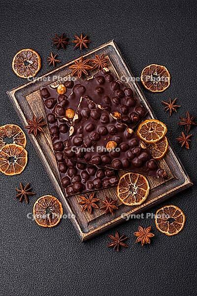 Food, Black bitter chocolate with whole hazelnuts, candied fruits and mint, broken into pieces on a dark concrete background [IBR124773744]