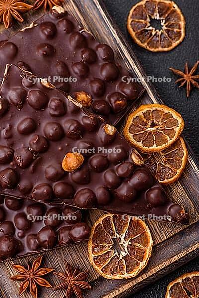 Food, Black bitter chocolate with whole hazelnuts, candied fruits and mint, broken into pieces on a dark concrete background [IBR124773745]