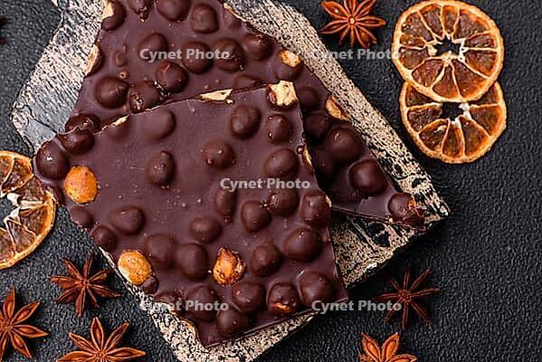 Food, Black bitter chocolate with whole hazelnuts, candied fruits and mint, broken into pieces on a dark concrete background [IBR124773746]