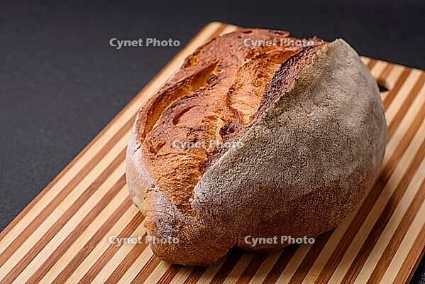 Food, A loaf of brown bread with grains of cereals on a wooden cutting board on a dark concrete background [IBR124773754]