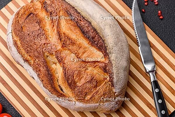 Food, A loaf of brown bread with grains of cereals on a wooden cutting board on a dark concrete background [IBR124773755]