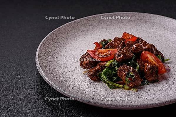 Food, Delicious warm salad with pieces of meat, spinach, tomatoes, salt, spices and herbs on a dark concrete background [IBR124773759]
