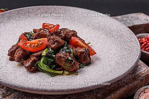 Food, Delicious warm salad with pieces of meat, spinach, tomatoes, salt, spices and herbs on a dark concrete background [IBR124773761]