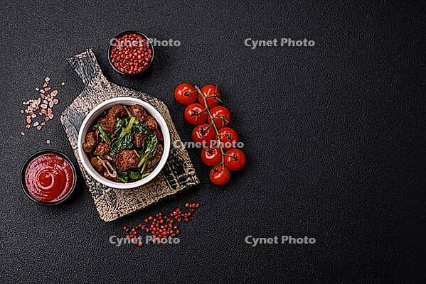 Food, Delicious warm salad with pieces of meat, spinach, tomatoes, salt, spices and herbs on a dark concrete background [IBR124773764]
