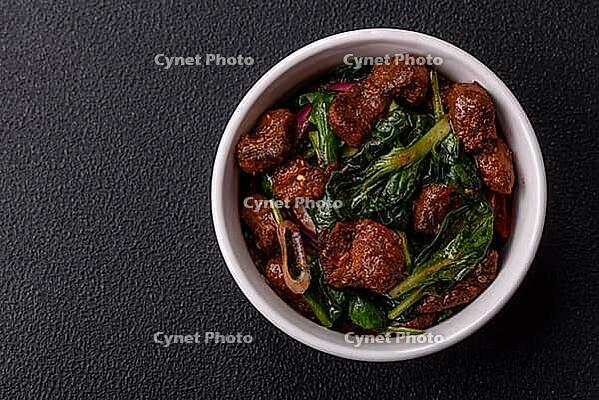 Food, Delicious warm salad with pieces of meat, spinach, tomatoes, salt, spices and herbs on a dark concrete background [IBR124773765]