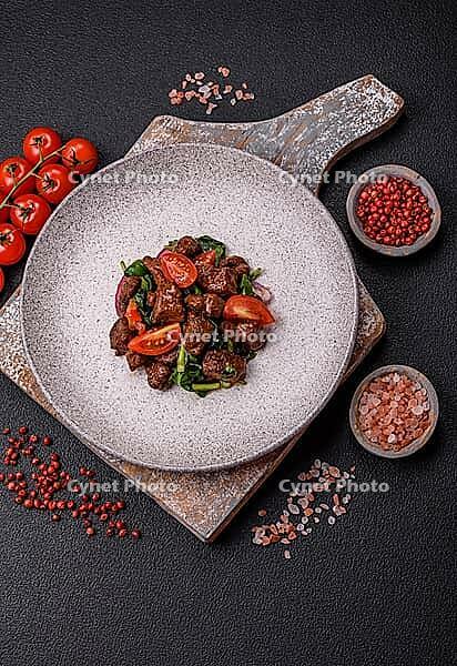 Food, Delicious warm salad with pieces of meat, spinach, tomatoes, salt, spices and herbs on a dark concrete background [IBR124773767]