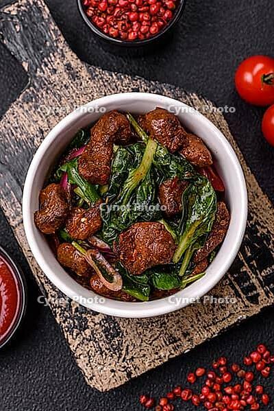 Food, Delicious warm salad with pieces of meat, spinach, tomatoes, salt, spices and herbs on a dark concrete background [IBR124773769]