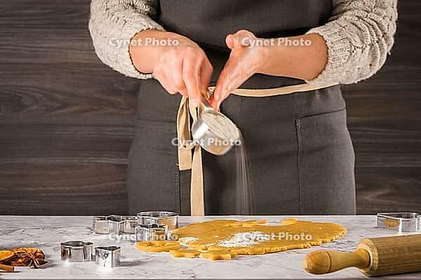 Female hands preparing Christmas cookies. Raw dough and cookie cutters on marble kitchen tabletop [IBR124817845]