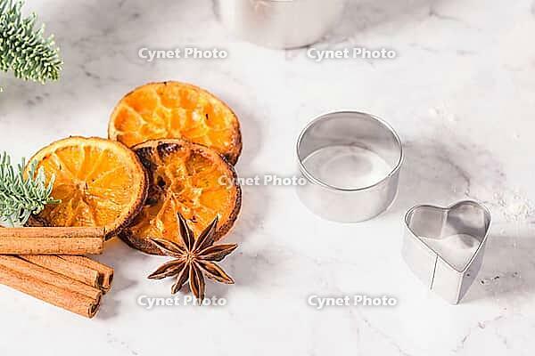 Slices of dried orange and a branch of pine Christmas cookies cutters on marble surface [IBR124817847]
