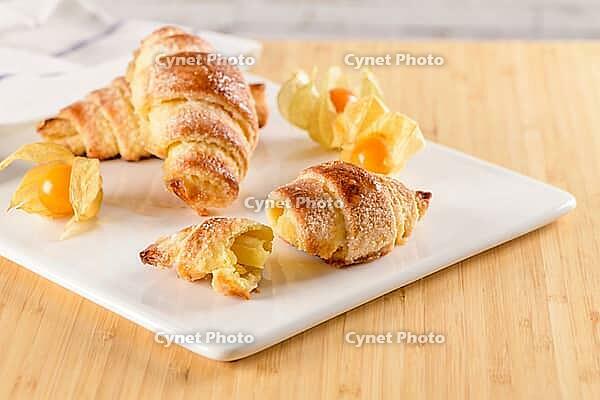 Small croissant with physalis fruits in white ceramic tray, homemade cakes on wooden table top [IBR124817892]