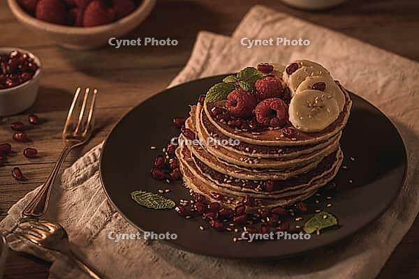 Pancakes with raspberries, banana slices, pomegranate seeds and honey on wooden vintage table [IBR124817902]