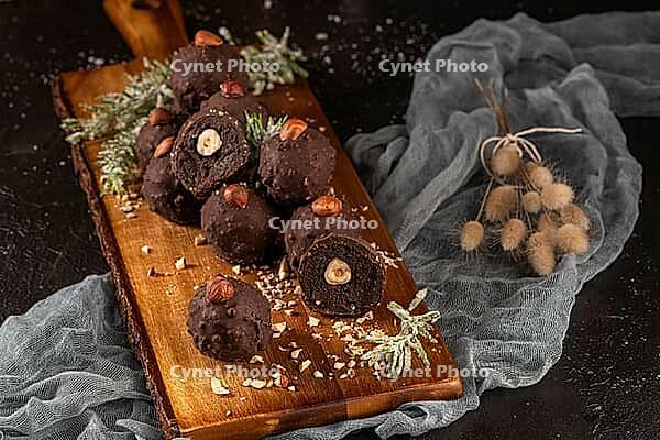 Dark chocolate truffles with hazelnuts over wooden cutting board [IBR124817908]