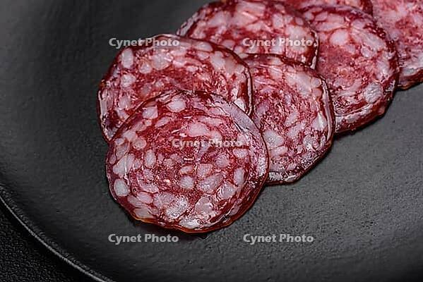 Food, Delicious smoked sausage with bacon, salt, spices and herbs cut into slices on a wooden cutting board [IBR124842039]