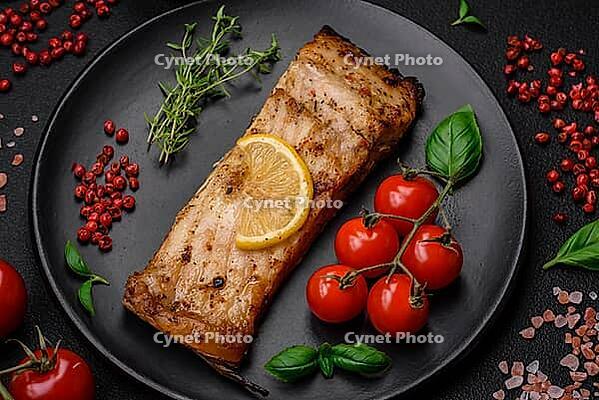 Food, Slice of delicious baked fish with salt, spices and herbs on a ceramic plate on a dark concrete background [IBR124842046]