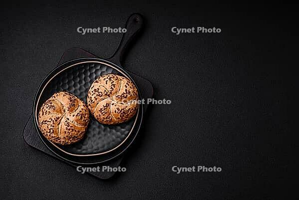 Food, Delicious freshly baked crispy bun or kaiser roll with sesame seeds on dark concrete background [IBR124842056]