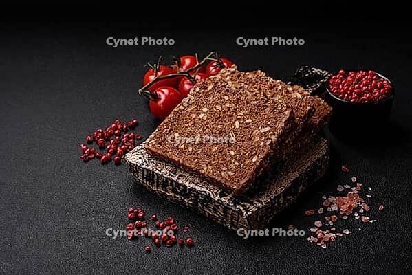 Food, Delicious fresh crispy brown bread with seeds and grains cut into slices on a dark concrete background [IBR124842059]