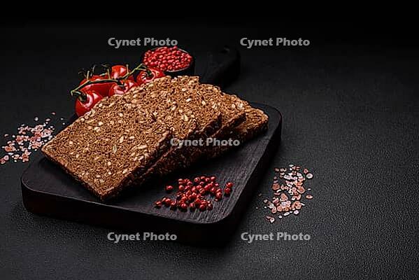 Food, Delicious fresh crispy brown bread with seeds and grains cut into slices on a dark concrete background [IBR124842060]