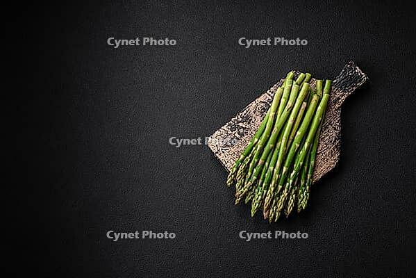 Food, Delicious fresh sprigs of asparagus on a dark textured background. Ingredients for a healthy vegetarian meal [IBR124842061]