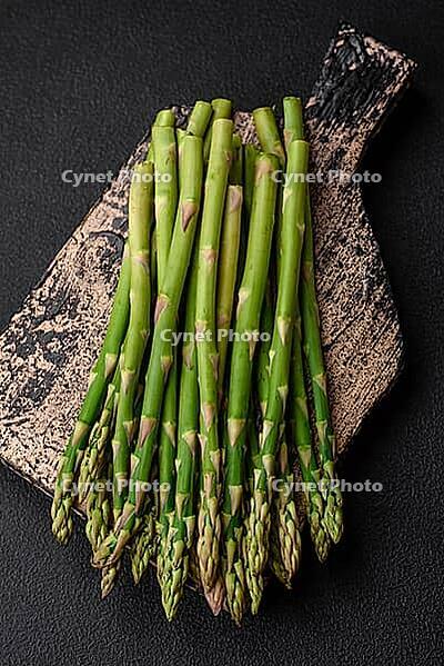 Food, Delicious fresh sprigs of asparagus on a dark textured background. Ingredients for a healthy vegetarian meal [IBR124842062]