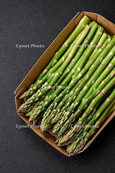 Food, Delicious fresh sprigs of asparagus on a dark textured background. Ingredients for a healthy vegetarian meal [IBR124842064]