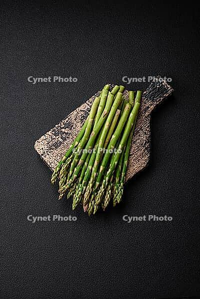 Food, Delicious fresh sprigs of asparagus on a dark textured background. Ingredients for a healthy vegetarian meal [IBR124842066]