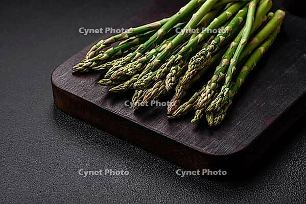 Food, Delicious fresh sprigs of asparagus on a dark textured background. Ingredients for a healthy vegetarian meal [IBR124842067]