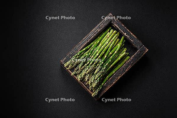 Food, Delicious fresh sprigs of asparagus on a dark textured background. Ingredients for a healthy vegetarian meal [IBR124842070]