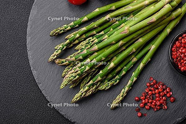 Food, Delicious fresh sprigs of asparagus on a dark textured background. Ingredients for a healthy vegetarian meal [IBR124842071]