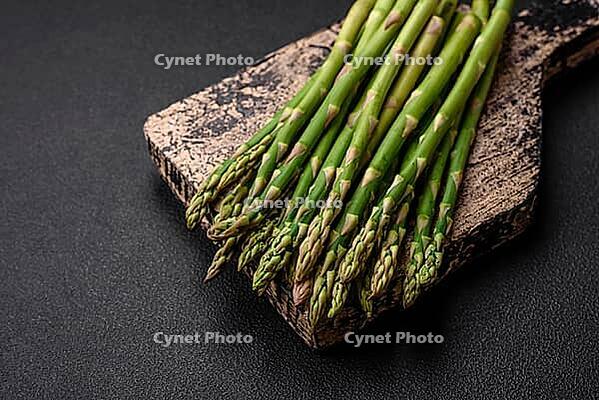 Food, Delicious fresh sprigs of asparagus on a dark textured background. Ingredients for a healthy vegetarian meal [IBR124842074]