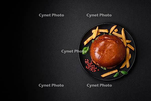 Food, Burger with juicy beef cutlet, cheese, tomatoes, salt, spices and herbs on a dark concrete background [IBR124842076]