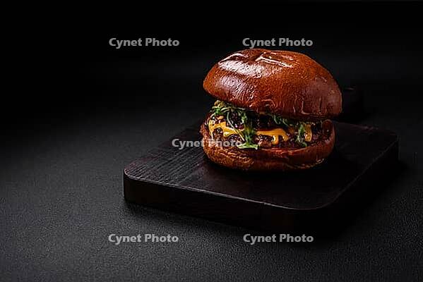Food, Burger with juicy beef cutlet, cheese, tomatoes, salt, spices and herbs on a dark concrete background [IBR124842080]