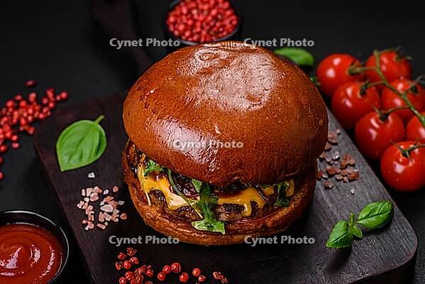 Food, Burger with juicy beef cutlet, cheese, tomatoes, salt, spices and herbs on a dark concrete background [IBR124842082]