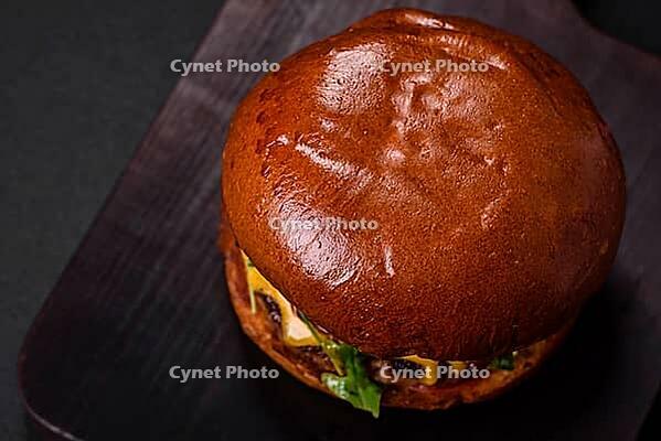 Food, Burger with juicy beef cutlet, cheese, tomatoes, salt, spices and herbs on a dark concrete background [IBR124842083]