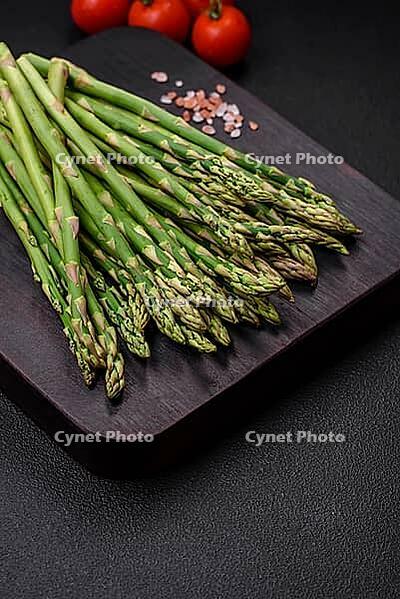 Food, Delicious fresh sprigs of asparagus on a dark textured background. Ingredients for a healthy vegetarian meal [IBR124842089]