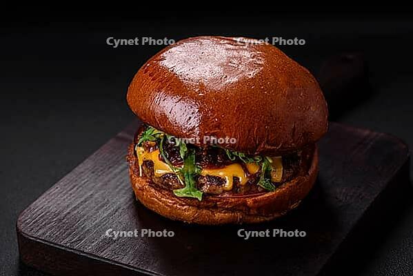 Food, Burger with juicy beef cutlet, cheese, tomatoes, salt, spices and herbs on a dark concrete background [IBR124842092]