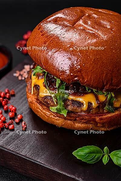 Food, Burger with juicy beef cutlet, cheese, tomatoes, salt, spices and herbs on a dark concrete background [IBR124842094]