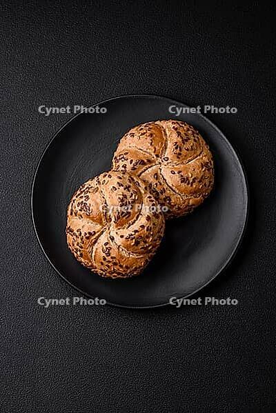 Food, Delicious freshly baked crispy bun or kaiser roll with sesame seeds on dark concrete background [IBR124842096]