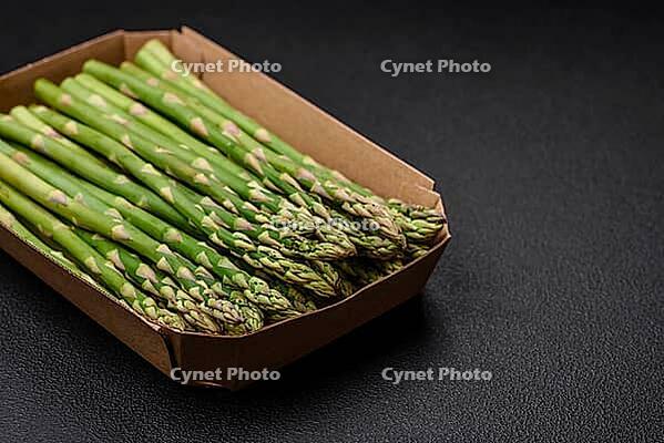 Food, Delicious fresh sprigs of asparagus on a dark textured background. Ingredients for a healthy vegetarian meal [IBR124842097]