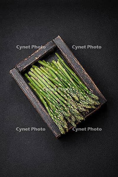 Food, Delicious fresh sprigs of asparagus on a dark textured background. Ingredients for a healthy vegetarian meal [IBR124842098]