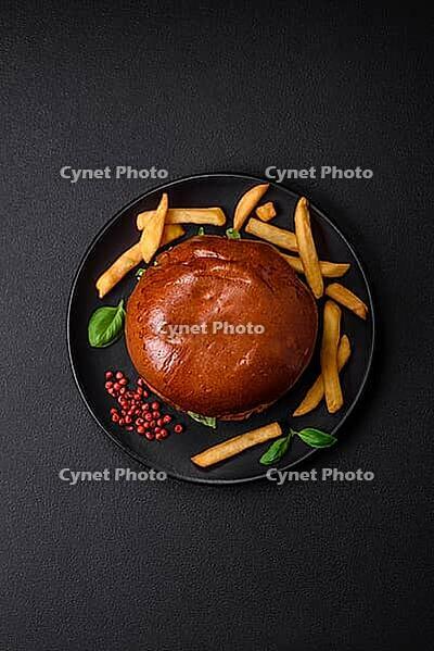 Food, Burger with juicy beef cutlet, cheese, tomatoes, salt, spices and herbs on a dark concrete background [IBR124842102]