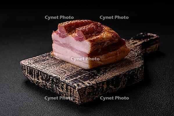 Food, Delicious calorie smoked bacon with salt, spices and herbs on a dark concrete background [IBR124842103]