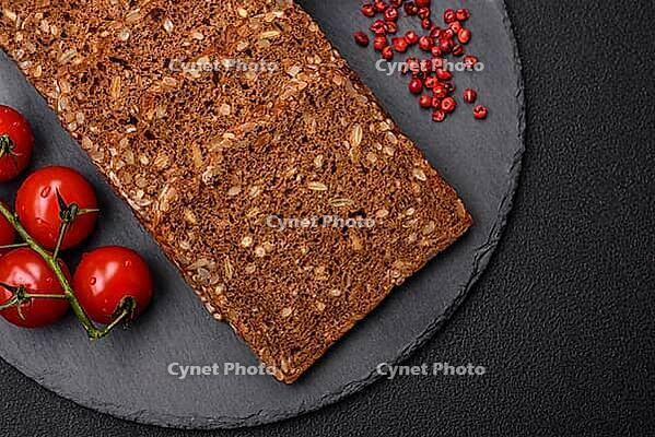 Food, Delicious fresh crispy brown bread with seeds and grains cut into slices on a dark concrete background [IBR124842108]