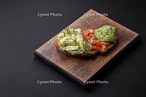 Food, Delicious brown bread toast with salmon, avocado, cucumber and sesame seeds on a textured concrete background [IBR124876413]