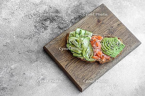 Food, Delicious brown bread toast with salmon, avocado, cucumber and sesame seeds on a textured concrete background [IBR124876416]