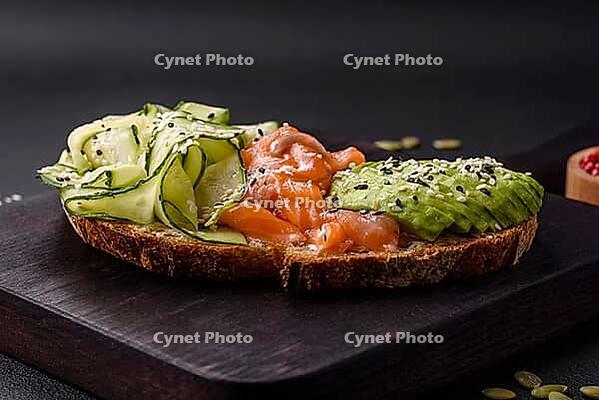 Food, Delicious brown bread toast with salmon, avocado, cucumber and sesame seeds on a textured concrete background [IBR124876418]