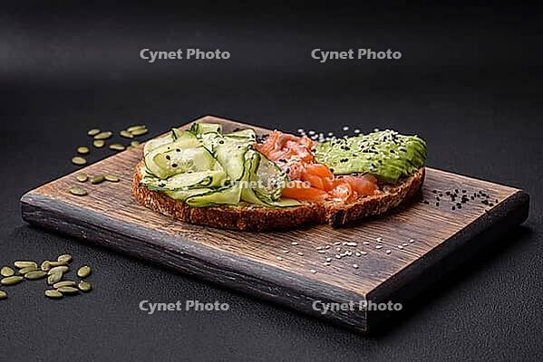 Food, Delicious brown bread toast with salmon, avocado, cucumber and sesame seeds on a textured concrete background [IBR124876419]