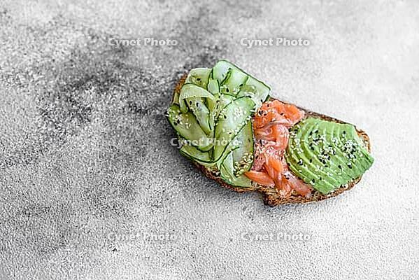 Food, Delicious brown bread toast with salmon, avocado, cucumber and sesame seeds on a textured concrete background [IBR124876420]