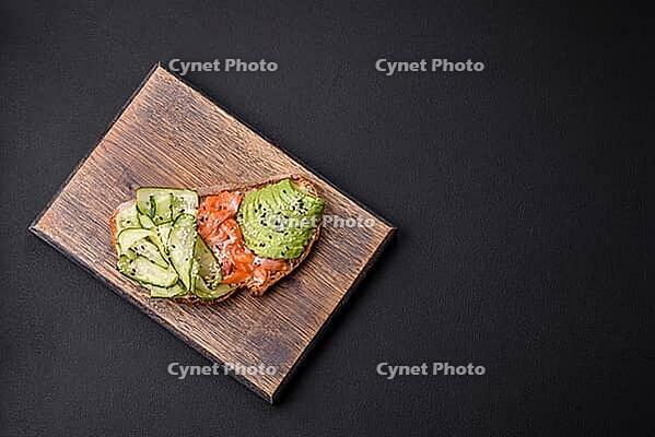 Food, Delicious brown bread toast with salmon, avocado, cucumber and sesame seeds on a textured concrete background [IBR124876421]