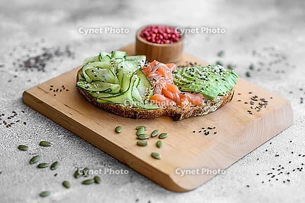 Food, Delicious brown bread toast with salmon, avocado, cucumber and sesame seeds on a textured concrete background [IBR124876422]